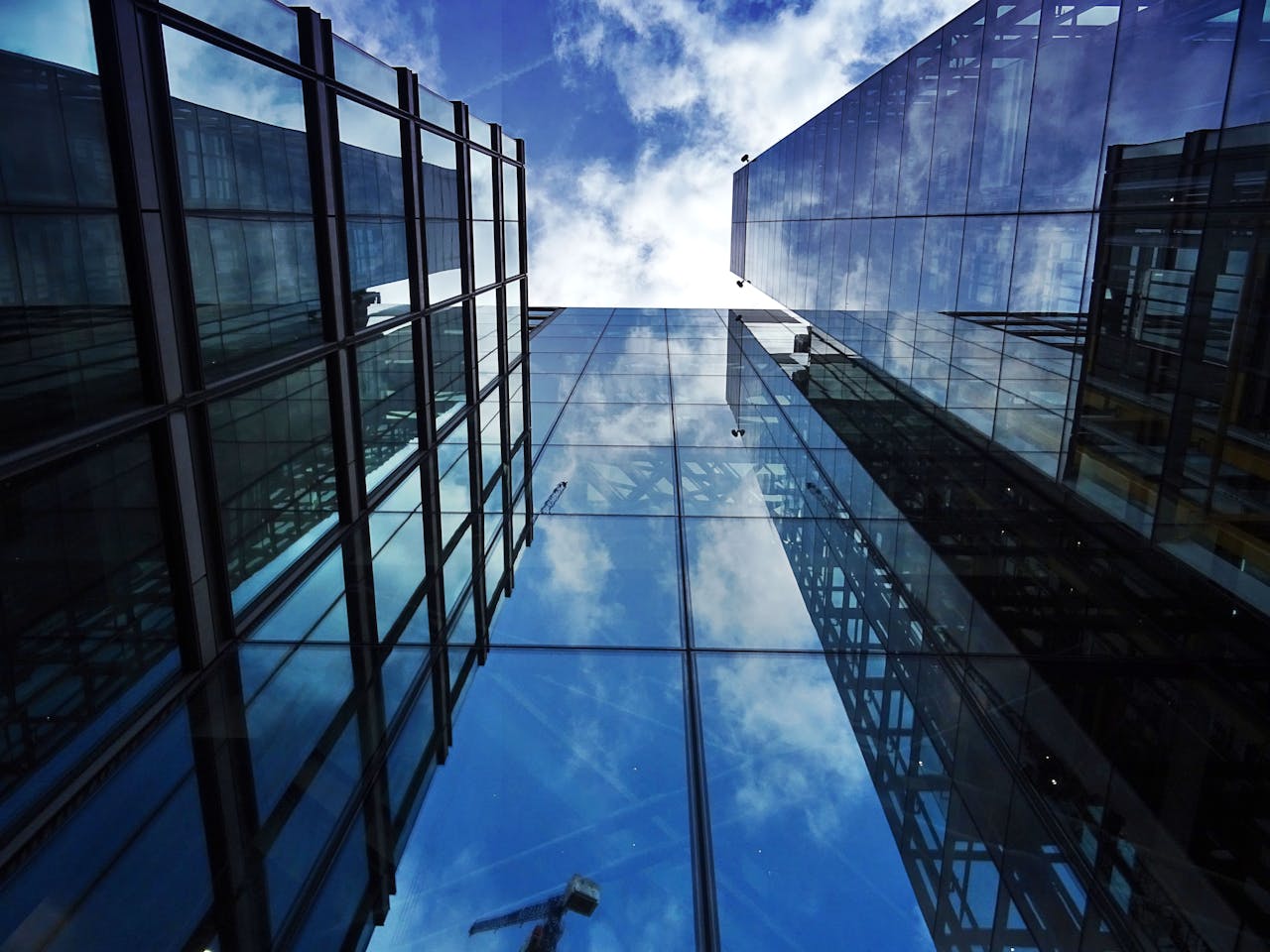Perspective view of modern skyscraper facades with glass reflections of clouds and sky.